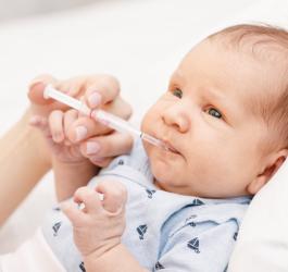 Mama podaje niemowlęciu lek przeciwgorączkowy za pomocą strzykawki.